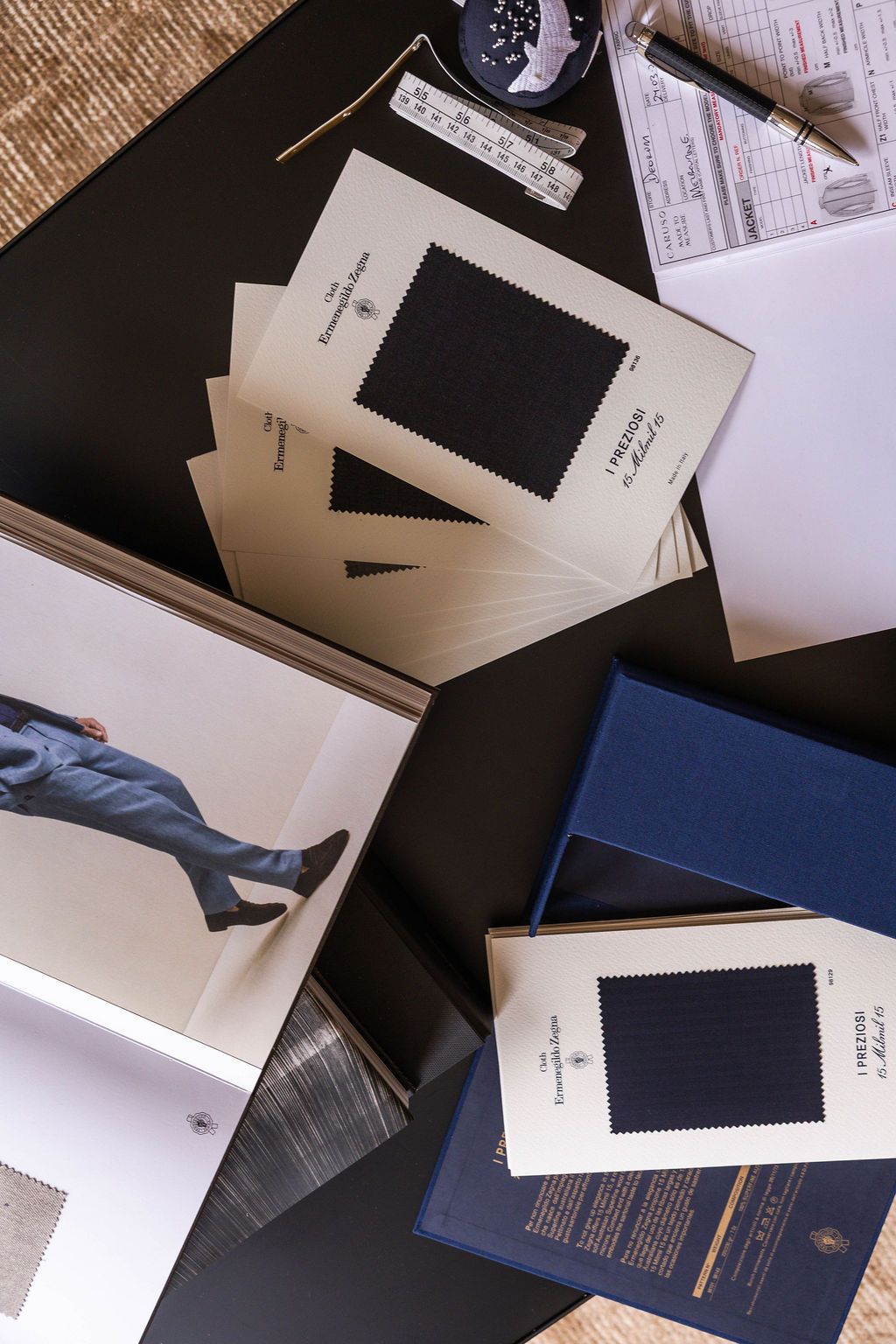 Close-up of a busy table with books, fabric swatches, designs and tailoring tools
